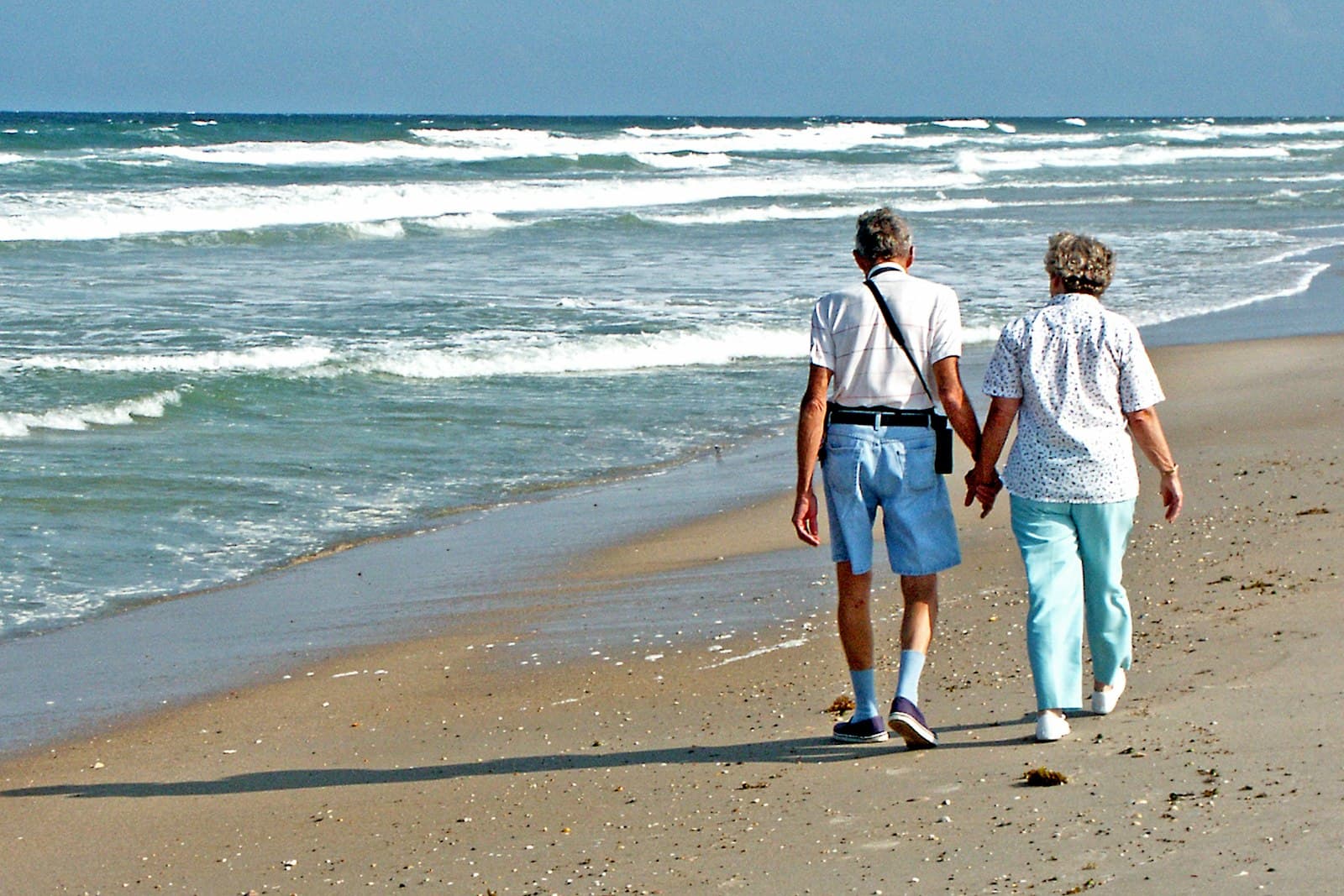 An older couple walking hand in hand along a beach